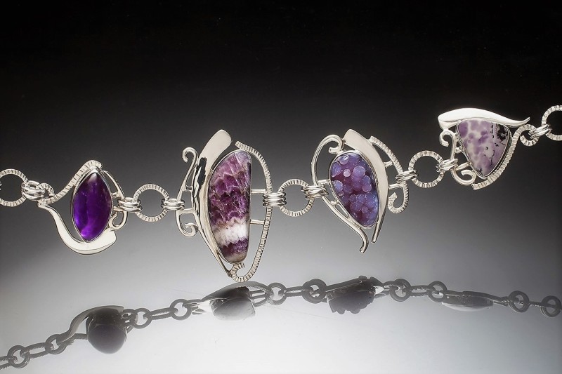 Closeup of purple gemstone jewelry with curved silver connected by smooth and ridged silver links. Created by Debbie Noiseux.