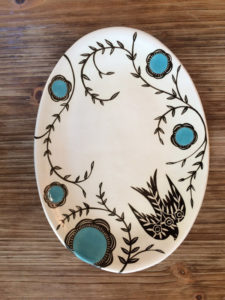 An oval platter with a black bird and blue flowers with black stems winding throughout the platter. Created by Dorrie Papademetriou