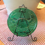 Green glass medallion with a crab motif by James Sharpless, displayed on a gingham table.