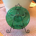 Green glass medallion with a crab motif by James Sharpless, displayed on a gingham table.