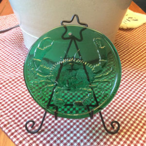 Green glass medallion with a crab motif by James Sharpless, displayed on a gingham table.
