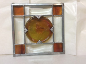 A glass panel with a crossed design and amber colored stained glass in each corner and a large amber color circle in the middle by James Sharpless