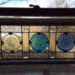 A glass panel with three circular glass medallions inside depicting a lighthouse, a shell, and a sand dollar by James Sharpless