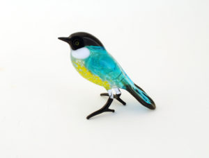 A flamework glass bird with a black head and blue and yellow body by Thomas Von Koch