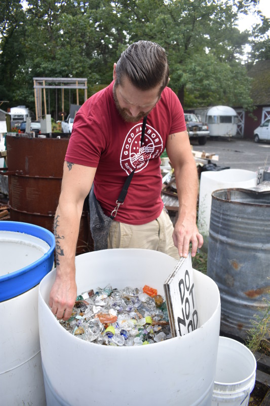 "Emanation 2019" Artist Jesse Krimes reaching into a large, round white bin full of broken glass pieces.