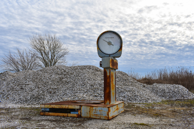 A large, rusted Fairbanks scale sits in front of a large hill of oyster shells.
