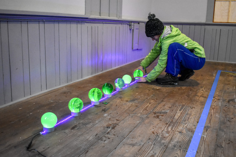 Intern Maddie Stewart neatly lines up small orbs glowing green with small strings of blacklight.