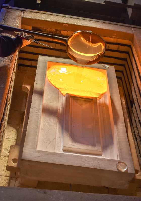A metal ladle is used to pour molten glass from our furnace into a pre-heated plaster mold of a door panel.