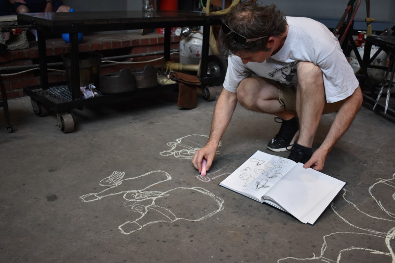 "Emanation 2019" Artist Tristin Lowe creates concept sketches in chalk on the floor of the Glass Studio. Sketches include different style bottles with wings.