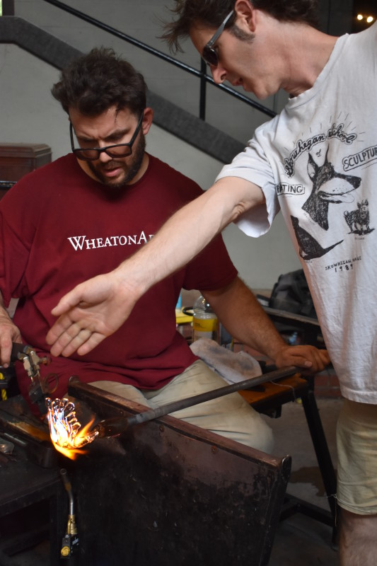 "Emanation 2019" Artist Tristin Lowe collaborates with WheatonArts Glass Artist Skitch Manion as he rolls and forms a piece of hot glass.