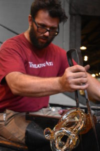 WheatonArts Glass Artist Skitch Manion shapes hot glass with large metal tweezers.