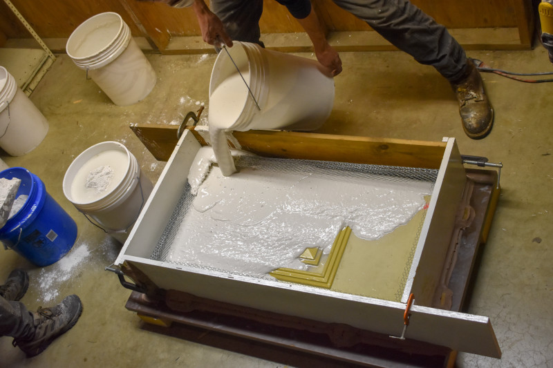 Glass Studio Artist pours a plaster mixture into the cottle board structure to create a mold of the door panel.