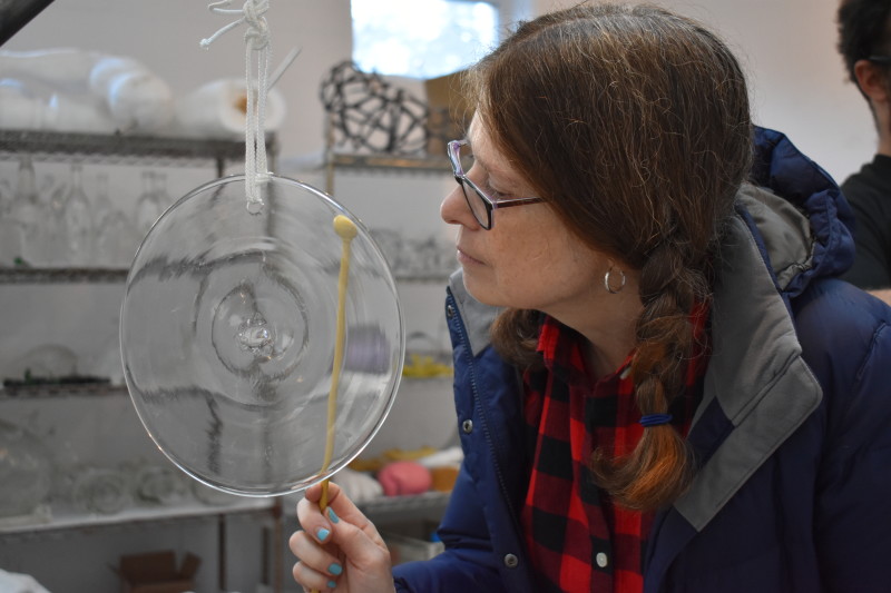 "Emanation 2019" Artist Laura Baird holds a small percussion mallet against a clear glass disc suspended by a white rope.