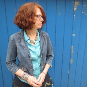 Laura Baird Head Shot in jean jacket with blue painted wood background