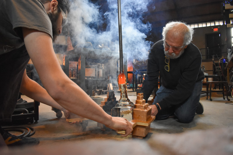 Emanation 2019 Artist Allan Wexler and WheatonArts Assistant Glass Artist Max Hertzan releasing a glass piece from its mold