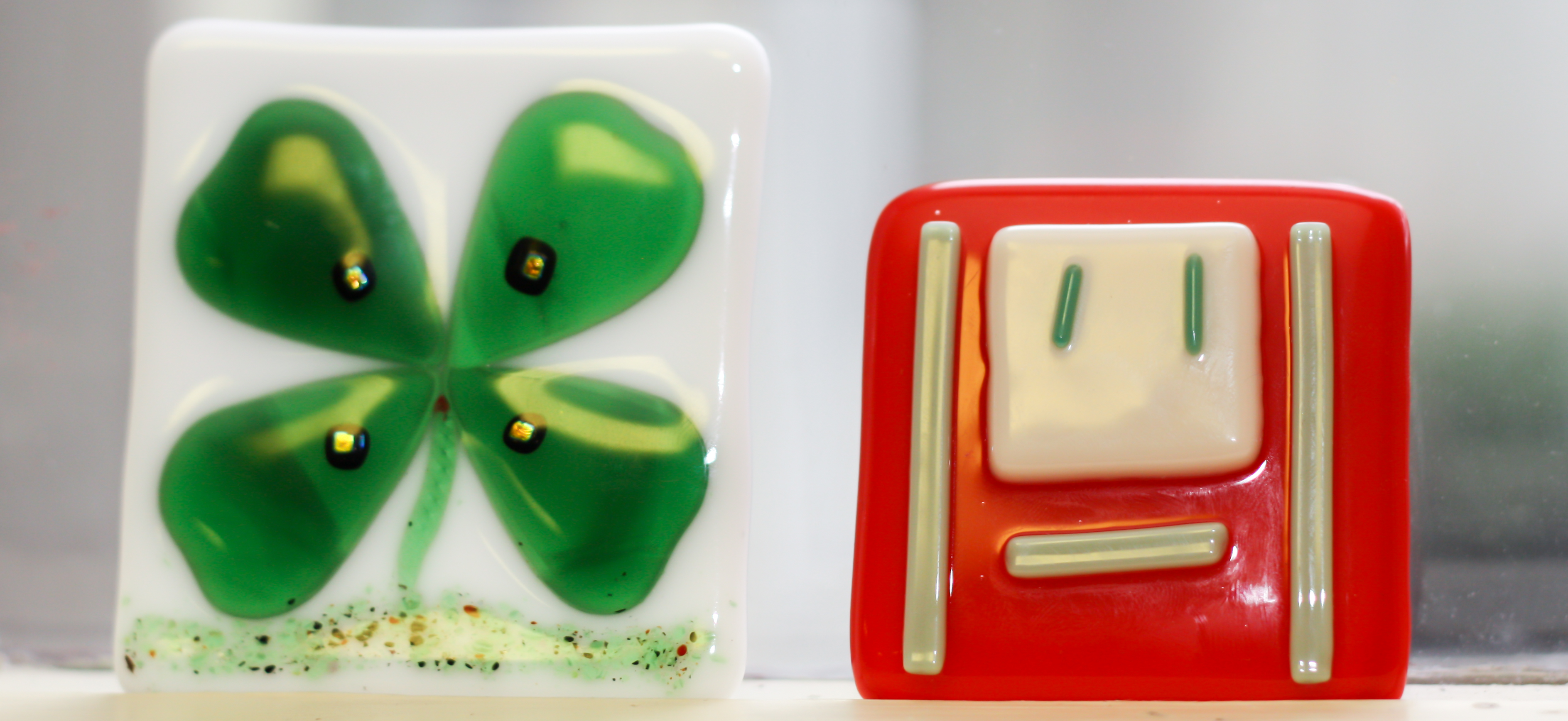 On left: White glass fused magnet with green clover design. On right: Red glass fused magnet with white rectangles of varying sizes.