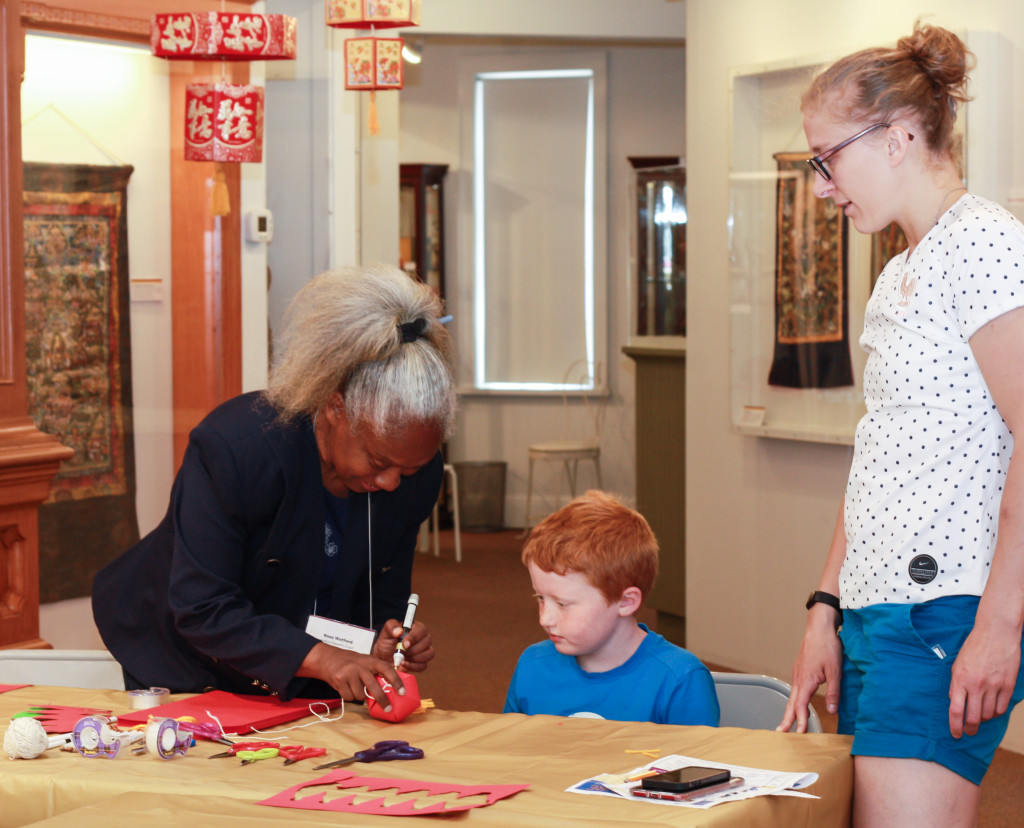 WheatonArts staff member Rosa assists a child and an adult creating paper lanterns in the Down Jersey Folklife Center at WheatonArts