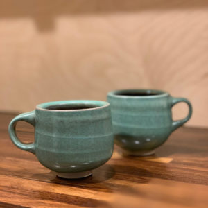 Two matching light teal mugs against a soft wooden background. Created by Samantha Bartlett