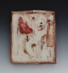A red sculpted clay bird sits on a white and red clay backdrop. Created by Priscilla Dahl.