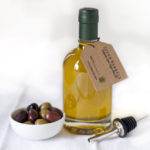A small bottle of olive oil from Seven Barrels with a spout to the right and a small dish of olives on the left