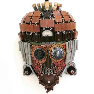 A found object mask by Larry Agnello, referencing masks from Africa. Red, yellow, and brown tiles fill its head and its chin is made with a small coocoo clock