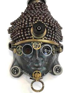 found object mask by Larry Agnello, referencing masks from Africa. Metal gears and rings adorn its deep green face,