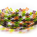 Green, purple, orange, and white bowl by Stephanie Baness formed with small overlapping glass squares of each color