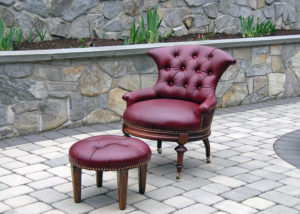 An elegant maroon chair and footrest on a stone floor. Created by Olya Bragger