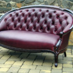 A burgundy sofa by Olya Bragger with a half circle top and deep brown armrests.