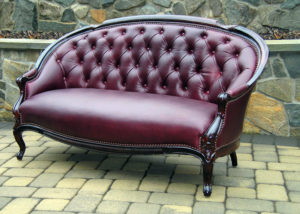 A burgundy sofa by Olya Bragger with a half circle top and deep brown armrests.