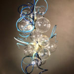 Hanging flamework sculpture by Stephen Brucker of several clear orbs with protruding light and dark blue spirals