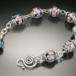 Bracelet by Sharon Carlucci with a silver chain and matching glass beads with iridescent floral designs.