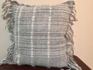 A grey pillow with fringe by Belinda DeCicco