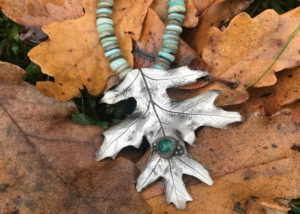 Silver metal clay leaf pendant with turquoise beads of various shades, laid on a bed of orange autumn leaves. Created by Sue Fontana.