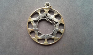Metal coin pendant carved by Allan Feinberg depicting five birds fly in a circle around the inside edge, creating a circle of negative space in the innermost center