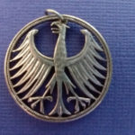 Metal coin pendant carved by Allan Feinberg depicting an angry bird, its wings spread open and talons bared.