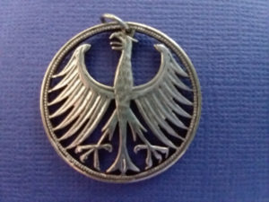 Metal coin pendant carved by Allan Feinberg depicting an angry bird, its wings spread open and talons bared.