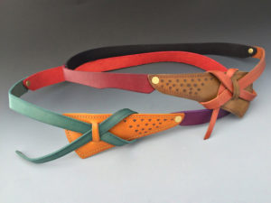 Two matching leather belts with separate color schemes, one black and red, the other purple, red, and teal. Created by Jorge Gil