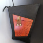 A midnight black asymmetrical leather bag with a smaller red pouch. Created by Jorge Gil
