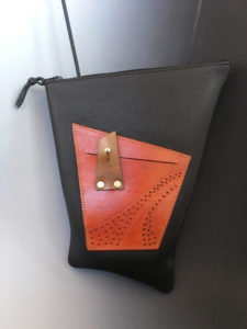 A midnight black asymmetrical leather bag with a smaller red pouch. Created by Jorge Gil