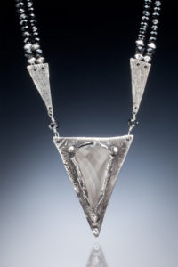 Necklace by Judith Hearney with a trangle pendant with a semi-precious faceted stone, hung either side by a smaller triangle and black beads