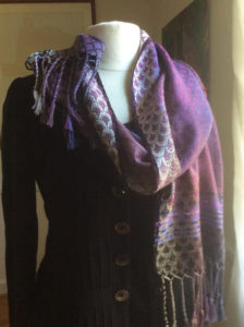 Purple scarf with a scale pattern wrapped loosely around a white mannequin form, by Maureen Kamerick