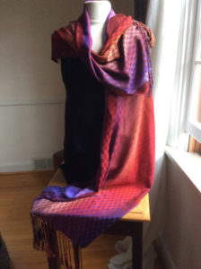Purple to red gradient checkerboard pattern scarf draped around a mannequin form and cascading down to the table it sits on. Created by Maureen Kamerick