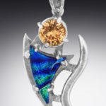 A silver pendant by Paul Lorber with a yellow gemstone and a swooping blue triangle stone dangling below