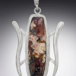 A silver pendant by Paul Lorber cradling a smooth brown oval gemstone