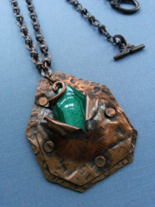 Textured copper pendant with a partially hidden green stone. Created by Kim Lyons