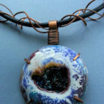 Blue pendant resembling a geode with peacock green stones within. Created by Kim Lyons