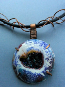 Blue pendant resembling a geode with peacock green stones within. Created by Kim Lyons