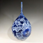 Blue ceramic piece by Erika Novak and Drew Darley with a wide body tapering to a long cylinder, cell-like silver and blue circles throughout the piece