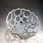 White and light blue decorative bowl by Erika Novak and Drew Darley with large oval holes of various sizes.